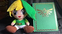 Link plush beside green hardcover guide showing gold Triforce