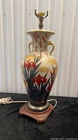 Full view of ceramic vase lamp on wood base with cord visible