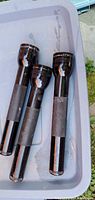 Three black MagLite flashlights inside plastic bin, showing full bodies