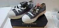 Pair of grey Converse sneakers on box showing sides and laces