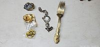 All items laid out: fork, pendant watch, cameo brooch, two rose brooches