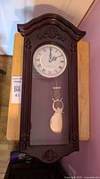 Front view of wooden wall pendulum clock showing full case, dial, pendulum