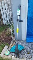 Full view of Yardworks electric trimmer leaning against shed with trimmer line spool at base