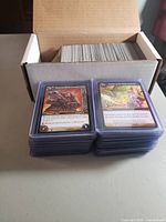 Cardboard storage box filled with unsleeved cards and two stacks of sleeved cards