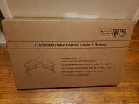 Sealed box labelled L-Shaped Desk Corner Table + Stand