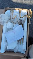 Boxed chandelier components with gold arms, downrods, styrofoam packing and folded instruction sheet