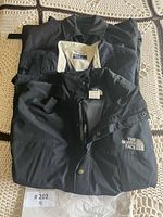 Stack of three jackets showing North Face logo, Polo tag, and third coat beneath