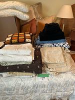 Overall lot showing stacks of towels, crochet blanket, duvet cover, quilts on bed