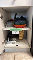 Cabinet shelf with Dutch oven, Denby casserole, frying pan, glass dish, baking sheets, Bundt pan, basket of small metal items