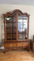 Front view of carved glass china cabinet showing doors, drawer, carvings
