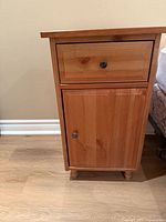 Front view of one pine bedside table showing drawer, cabinet door, knobs and feet