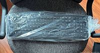 Black full-size computer keyboard sealed in plastic on office chair