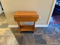 Front view of wooden drop-leaf side table showing lowered leaves, curved supports, lower shelf
