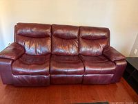 Front view of three-seat cranberry leather reclining couch against wall