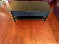 Full view of black IKEA coffee table showing split hinged top, storage capability and lower shelf
