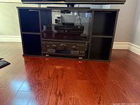 Front view of black TV stand showing compartments and glass door