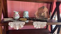 Overview of shelf with porcelain pieces, eyeglasses, grooming tools and doilies