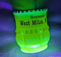 Toothpick holder glowing bright green under UV showing souvenir lettering and scalloped rim