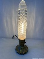 Full view of illuminated lamp showing glass column and metal base