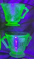 Front view of sugar and creamer under UV showing green glow and floral pattern