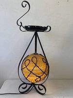 Full view of wrought iron lamp with lit globe shade and ashtray top