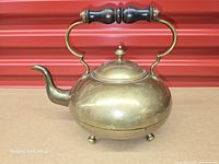 Left profile of brass kettle showing spout, handle, feet, lid