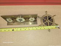 Top view showing both brass weather station and ship-wheel pen holder with tape measure for scale