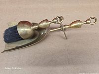 Brush resting inside brass dustpan, angled view