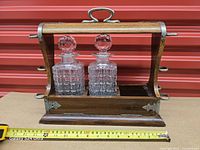 Front view of wood tantalus with both decanters in place, tape measure shows width