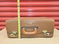 Front view of suitcase showing handle, locks, and measuring tape for height reference.