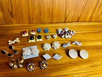 Overview of all fourteen earring pairs on wooden surface