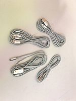 Four coiled silver braided USB-A to Lightning cables on white surface