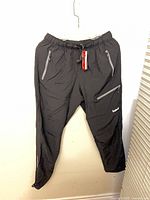 Full front view of Balear black rain pants hanging, showing pockets and overall design
