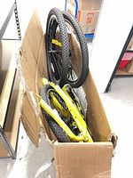 Open cardboard box showing yellow tricycle frame and black wheels