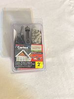 Front view of sealed Cortex fastening kit showing screws, plugs, tool and label