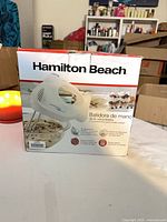 Front of boxed Hamilton Beach 6-speed hand mixer showing product image and Spanish text