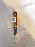 Front view of orange/black LCD voltage tester pen inside clear plastic bag