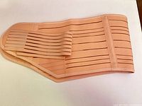 Full view of peach nude postpartum abdominal binder laid flat showing ribbed elastic and Velcro strap