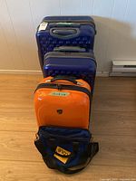 Group shot of two blue Heys suitcases, orange carry-on and blue Lole bag