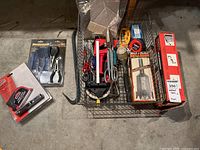 Overview of wire basket with assorted tools, packaged laser level, mini plier set, Ramset tool box