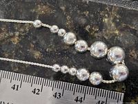 Top view showing graduated polished beads on chain beside ruler for scale