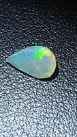 Pear-shaped faceted opal on textured background showing play-of-color