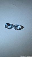 Two oval faceted aquamarines on neutral background