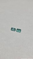 Pair of emerald cut green gemstones on neutral background