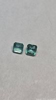 Both octagon-cut emeralds side by side on neutral background
