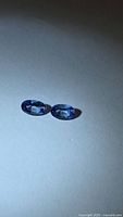 Two oval blue-purple gemstones on neutral background
