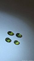 Four oval faceted green/yellow sapphires under angled light