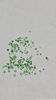 Cluster of many small green round faceted gemstones on neutral background