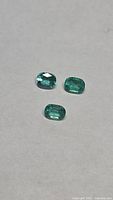 Three loose green cushion-cut emeralds on neutral background