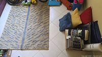 Area rug on floor with assorted pillows stacked nearby
